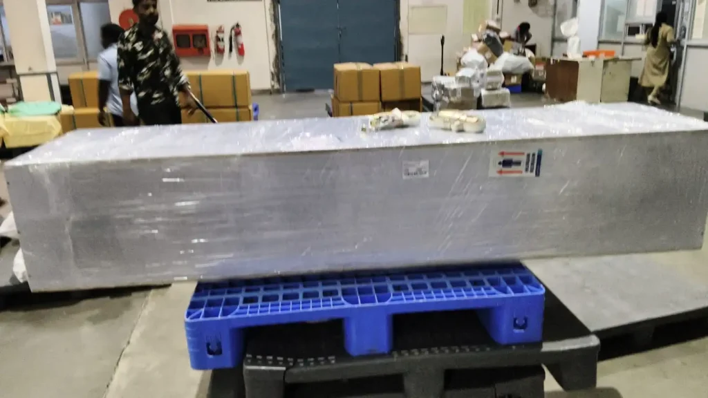 Airline-approved rectangular wooden coffin securely shrink-wrapped on a blue cargo pallet waiting for flight loading
