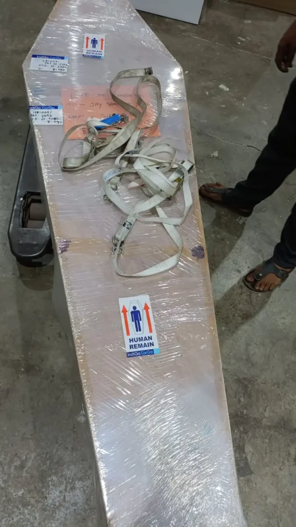 Shrink-wrapped hexagonal wooden coffin secured with heavy-duty cargo straps and IndiGo CarGo human remains labels